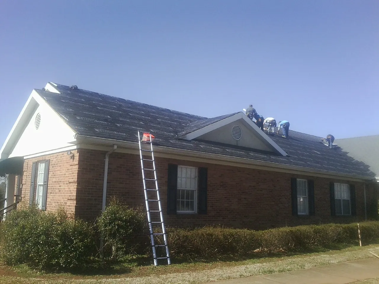 Crew tearing shingles off a brick ranch roof with a ladder set — Metal Roof Repair work by our crew in Mountlake Terrace
