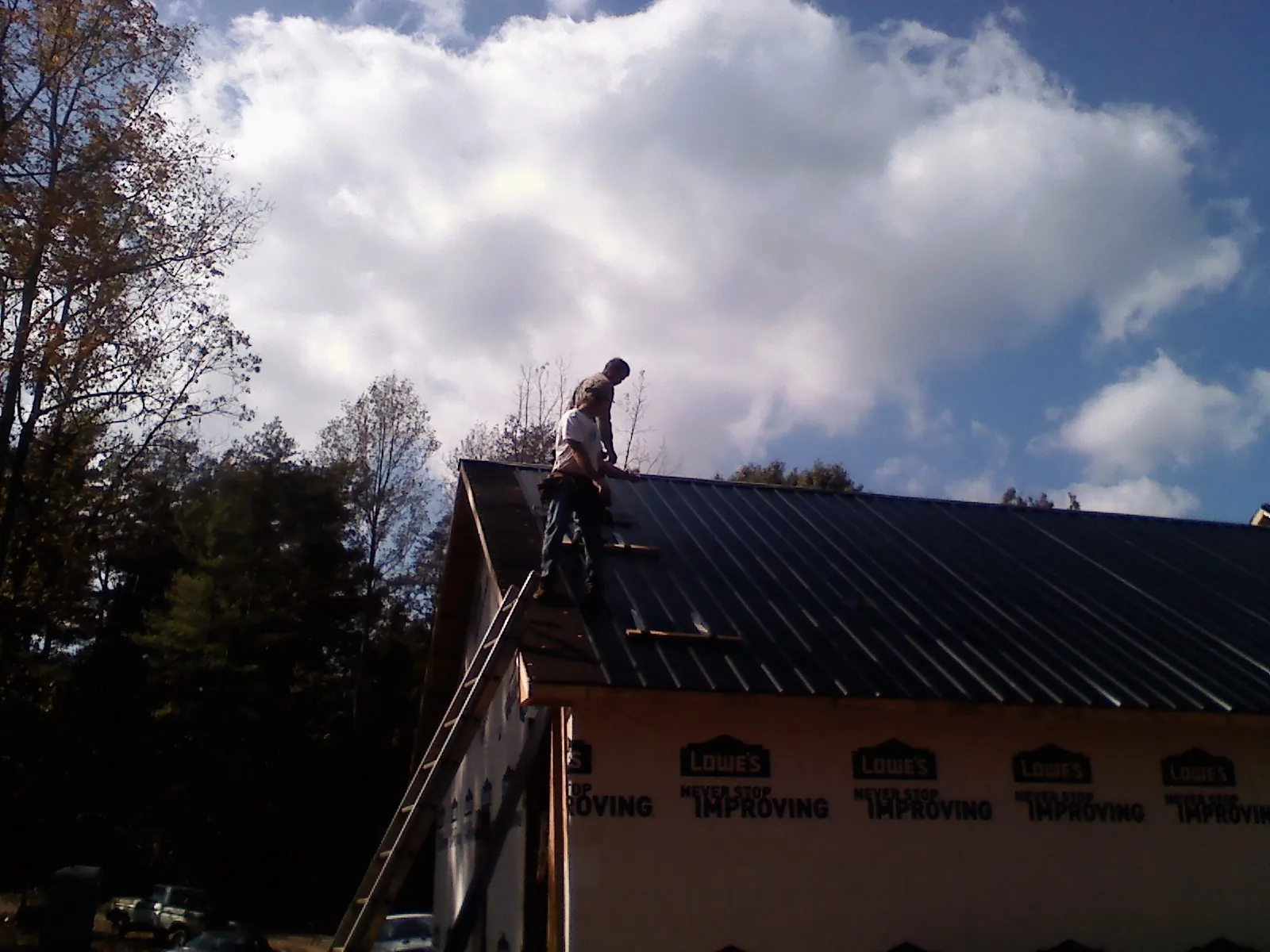Roofer fastening dark metal panels high against a cloudy sky, from a Roof Inspection job in Mountlake Terrace
