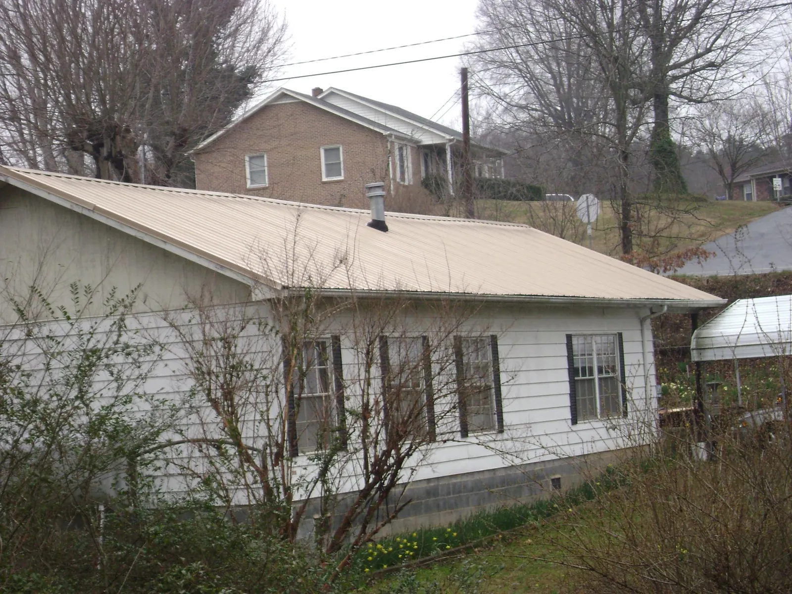Tan metal roof on a white sided house set into a hillside — Commercial Roofing by Roofing Brothers in Mountlake Terrace